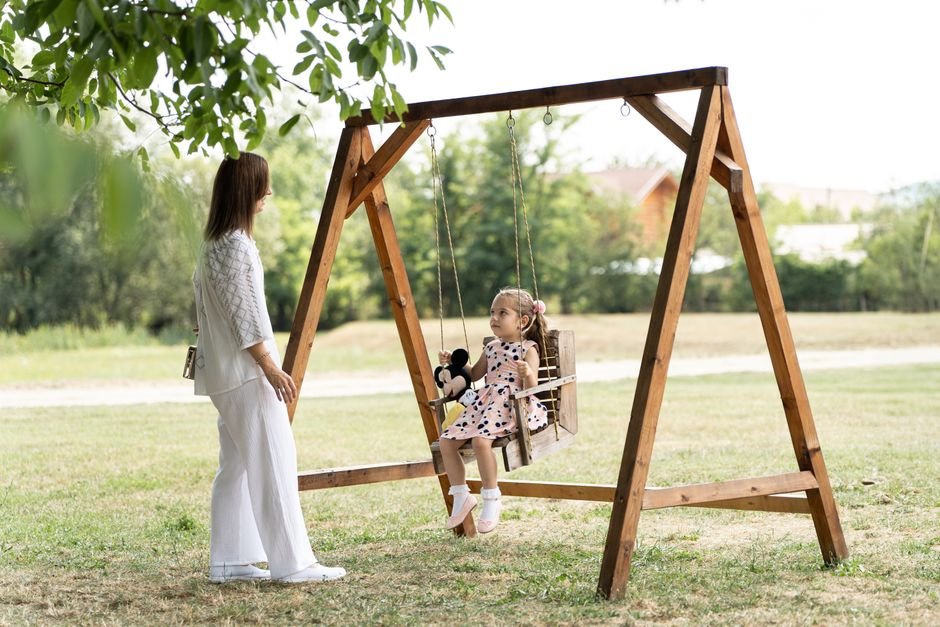 Mama ir dukra sūpuojasi medinėse sūpynėse, mėgaudamos ramiu laiku parke