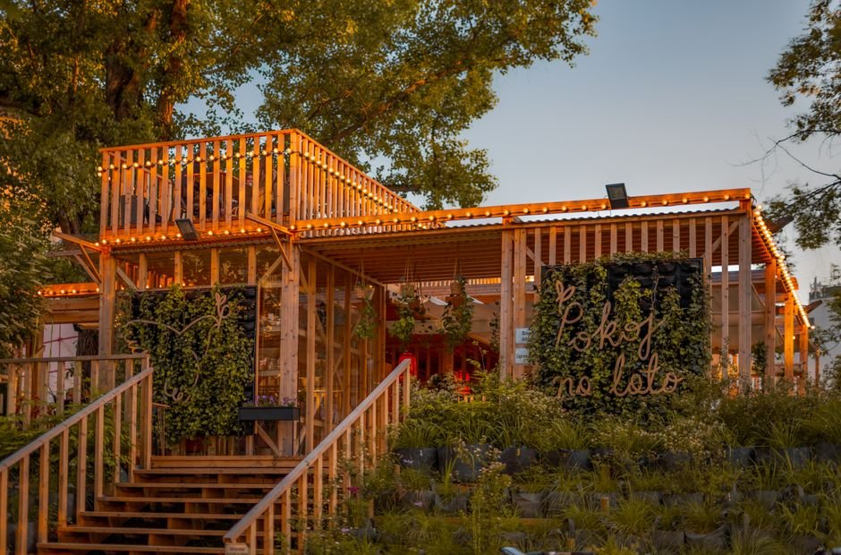 Medinis lauko paviljionas su girliandomis saulėlydžio metu – puiki erdvė moksleivių kūrybai